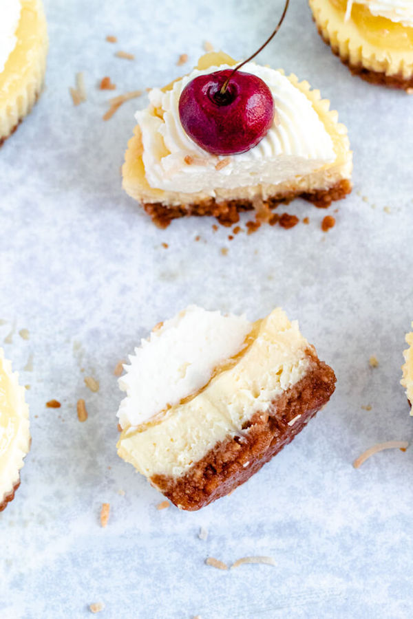 mini piña colada cheesecakes with pineapple sauce, coconut whipped cream, toasted coconut and a cherry on top.