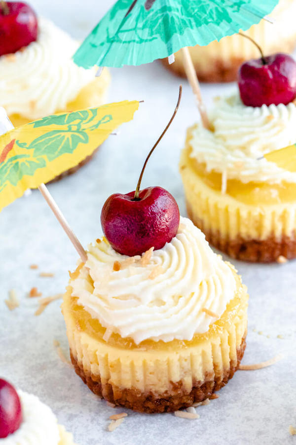 mini piña colada cheesecakes with pineapple sauce, coconut whipped cream, toasted coconut and a cherry on top.