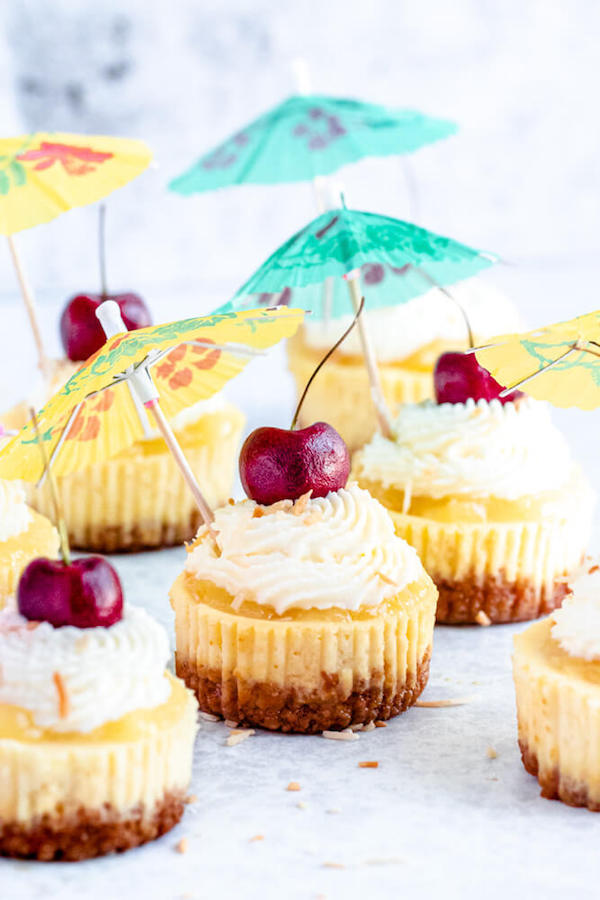 mini piña colada cheesecakes with pineapple sauce, coconut whipped cream, toasted coconut and a cherry on top.