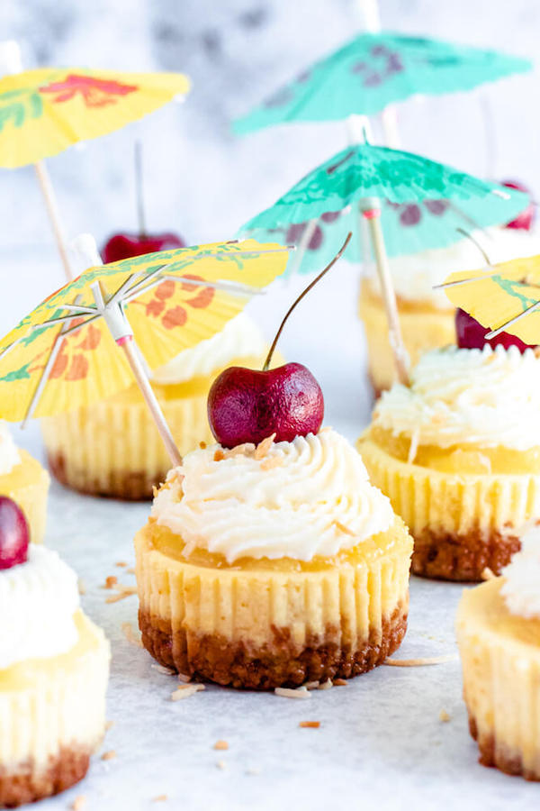 mini piña colada cheesecakes with pineapple sauce, coconut whipped cream, toasted coconut and a cherry on top.