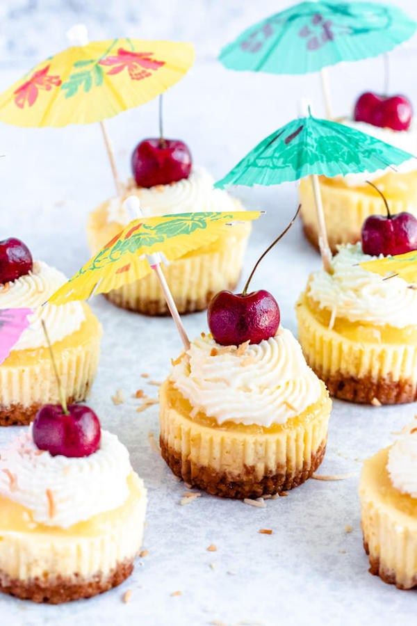 mini piña colada cheesecakes with pineapple sauce, coconut whipped cream, toasted coconut and a cherry on top.