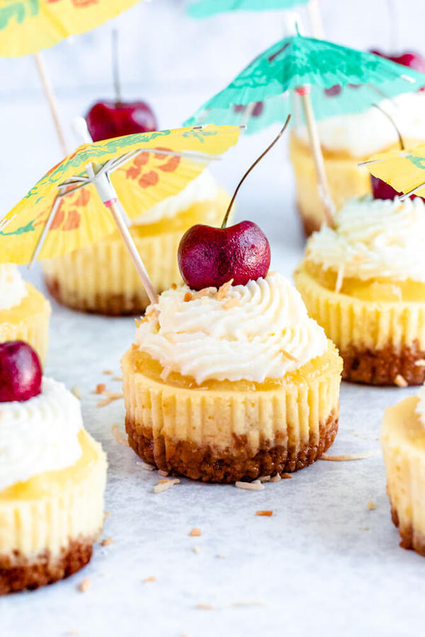 mini piña colada cheesecakes with pineapple sauce, coconut whipped cream, toasted coconut and a cherry on top.