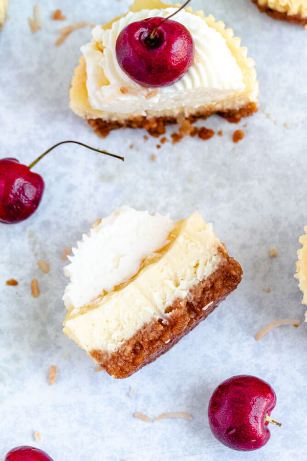 mini piña colada cheesecakes with pineapple sauce, coconut whipped cream, toasted coconut and a cherry on top.