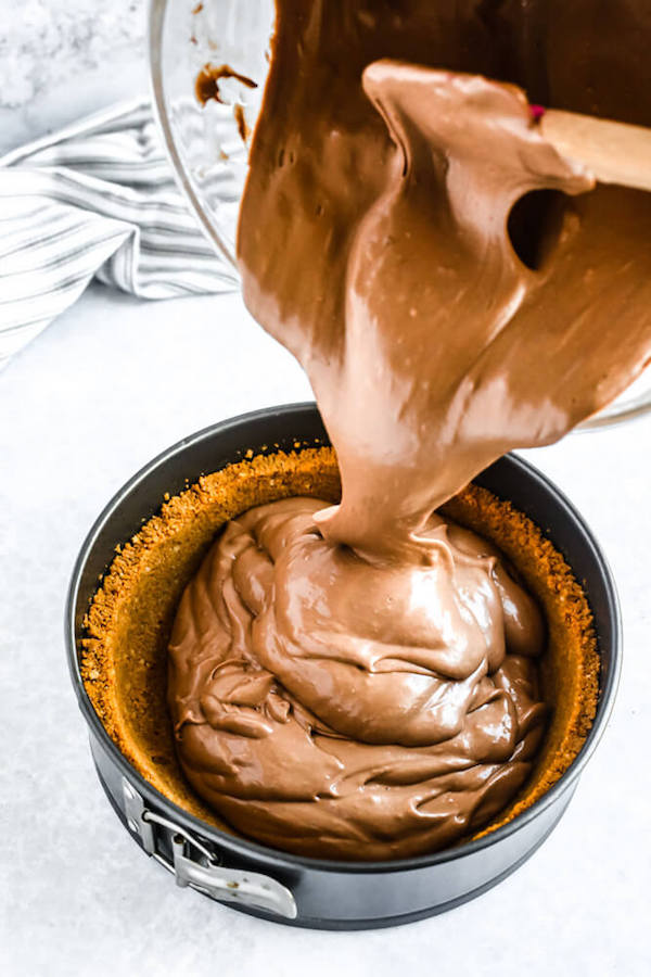 pouring chocolate cheesecake into graham cracker crust