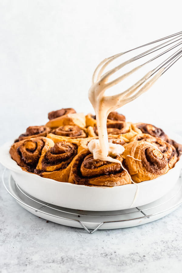 pouring browned butter cream cheese icing onto freshly baked pumpkin cinnamon rolls