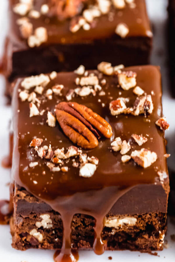 brownies with chocolate chips and chopped pecans baked inside and topped with chocolate fudge, salted caramel sauce and chopped pecans