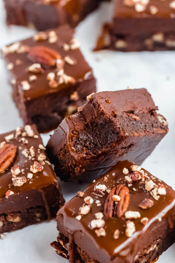 brownies with chocolate chips and chopped pecans baked inside and topped with chocolate fudge, salted caramel sauce and chopped pecans