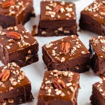 brownies with chocolate chips and chopped pecans baked inside and topped with chocolate fudge, salted caramel sauce and chopped pecans