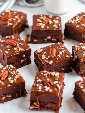 brownies with chocolate chips and chopped pecans baked inside and topped with chocolate fudge, salted caramel sauce and chopped pecans