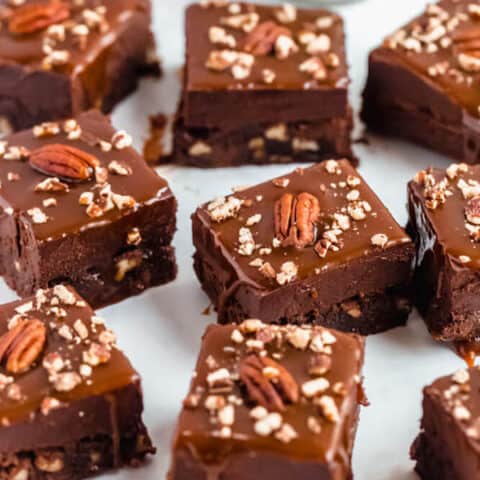 brownies with chocolate chips and chopped pecans baked inside and topped with chocolate fudge, salted caramel sauce and chopped pecans
