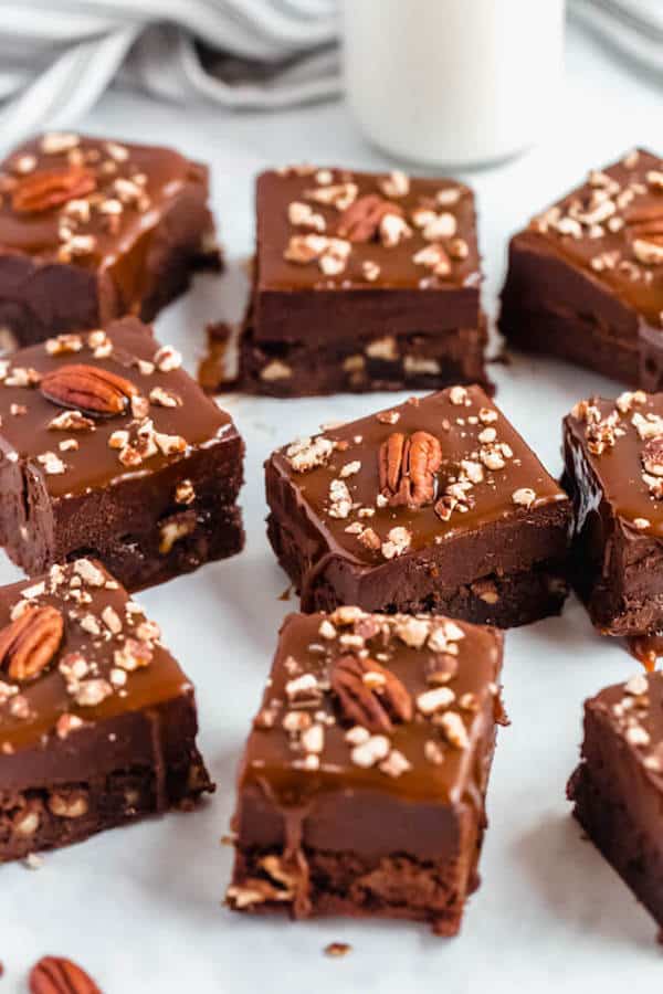 brownies with chocolate chips and chopped pecans baked inside and topped with chocolate fudge, salted caramel sauce and chopped pecans