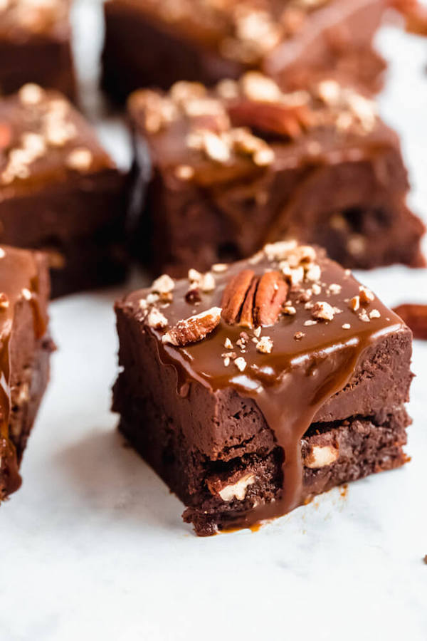 brownies with chocolate chips and chopped pecans baked inside and topped with chocolate fudge, salted caramel sauce and chopped pecans