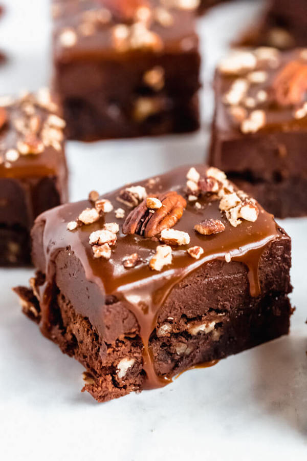 brownies with chocolate chips and chopped pecans baked inside and topped with chocolate fudge, salted caramel sauce and chopped pecans