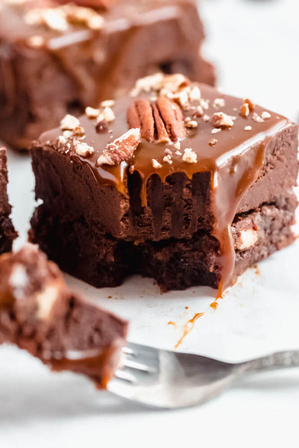 brownies with chocolate chips and chopped pecans baked inside and topped with chocolate fudge, salted caramel sauce and chopped pecans