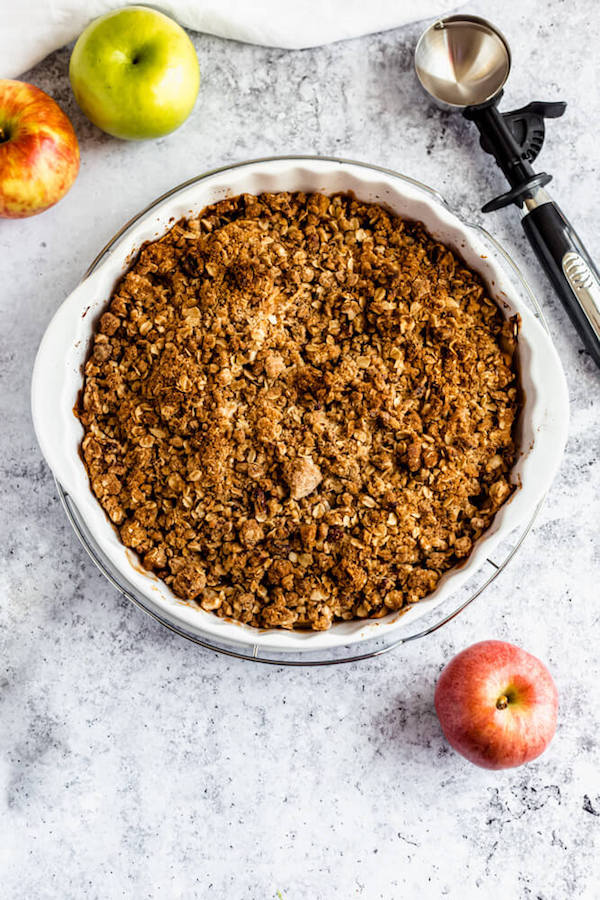 baked apple crisp surrounded by apples, spoons and an ice cream scoop