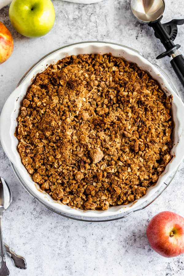 baked apple crisp surrounded by apples, spoons and an ice cream scoop