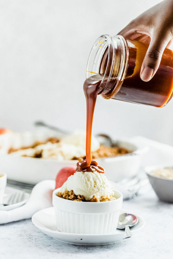 pouring salted caramel sauce onto apple crisp topped with vanilla ice cream