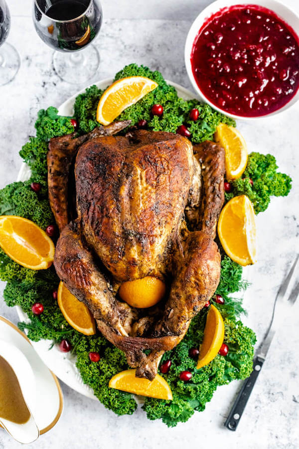 roasted turkey on a decorative turkey platter with a bowl of cranberry sauce on the side