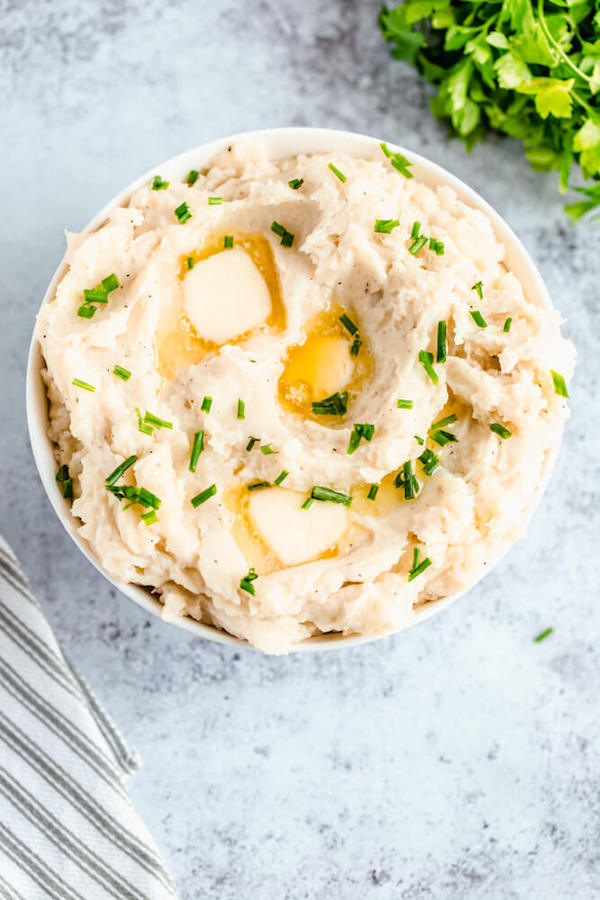 a bowl of mashed potatoes garnished with pieces of butter and chopped fresh chives