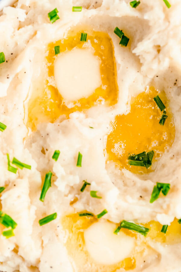 close up of mashed potatoes garnished with pieces of butter and chopped fresh chives