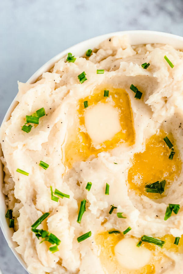 a bowl of mashed potatoes garnished with pieces of butter and chopped fresh chives