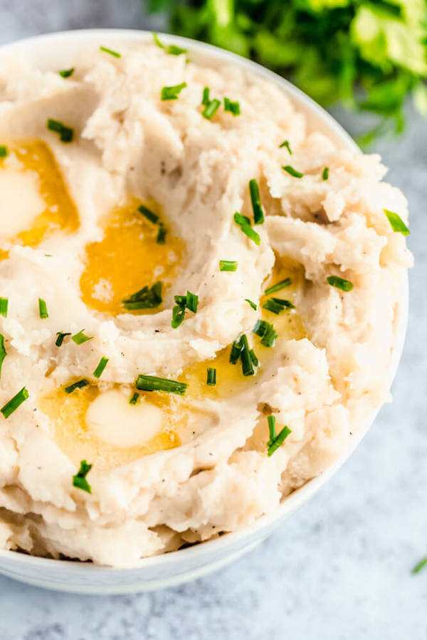 a bowl of mashed potatoes garnished with pieces of butter and chopped fresh chives