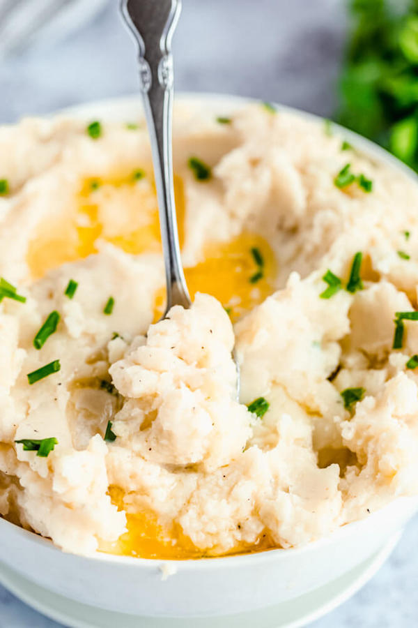 a bowl of mashed potatoes garnished with pieces of butter and chopped fresh chives