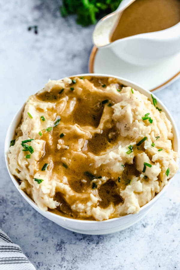 a bowl of mashed potatoes garnished with pieces of butter, chopped fresh chives and gravy