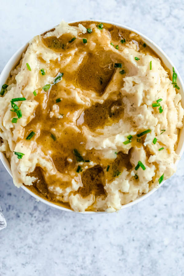 a bowl of mashed potatoes garnished with pieces of butter, gravy and chopped fresh chives