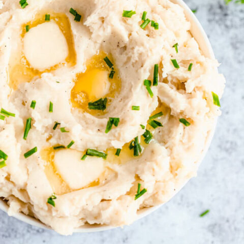 a bowl of mashed potatoes garnished with pieces of butter and chopped fresh chives