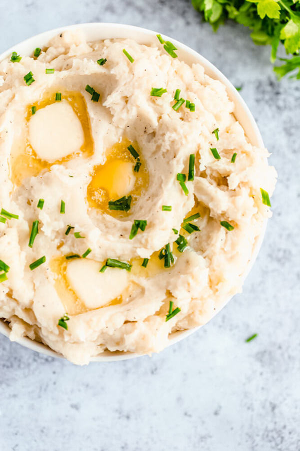 a bowl of mashed potatoes garnished with pieces of butter and chopped fresh chives