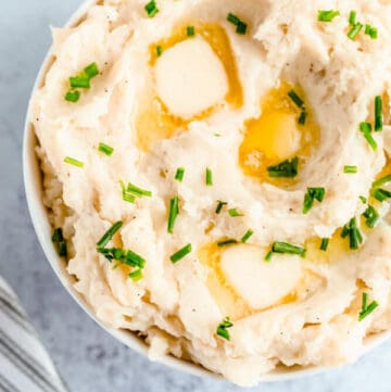 a bowl of mashed potatoes garnished with pieces of butter and chopped fresh chives