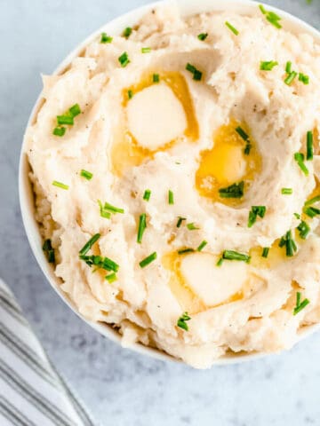 a bowl of mashed potatoes garnished with pieces of butter and chopped fresh chives