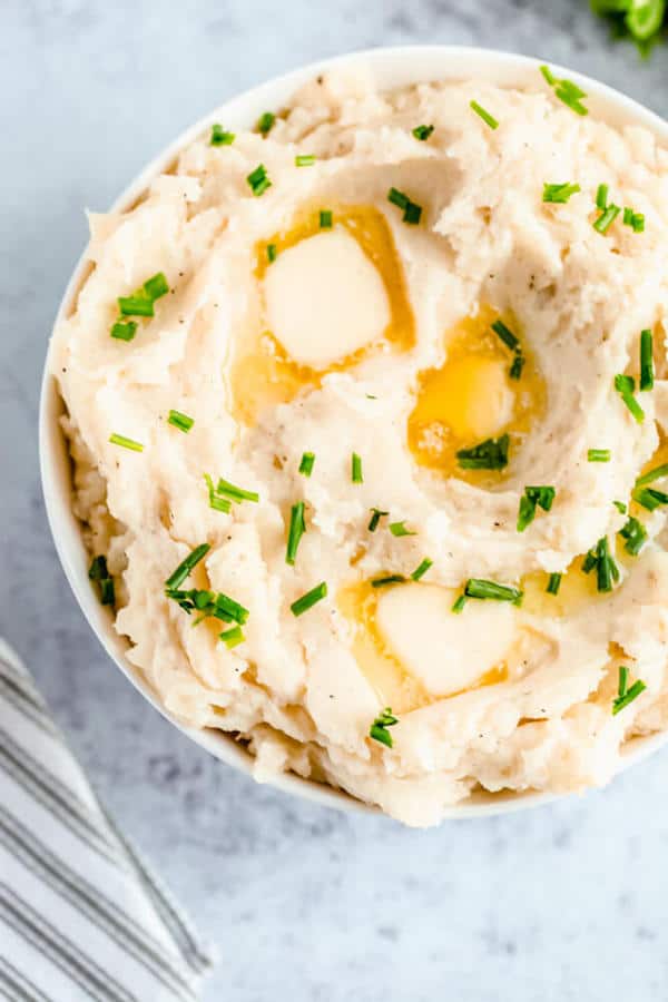 a bowl of mashed potatoes garnished with pieces of butter and chopped fresh chives