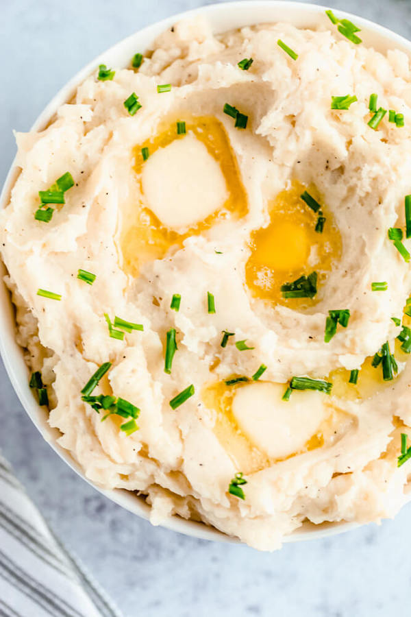 a bowl of mashed potatoes garnished with pieces of butter and chopped fresh chives