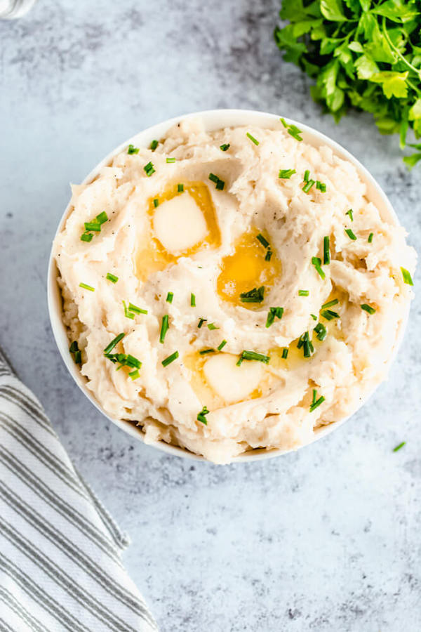 a bowl of mashed potatoes garnished with pieces of butter and chopped fresh chives