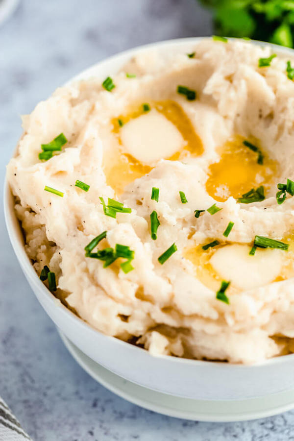 a bowl of mashed potatoes garnished with pieces of butter and chopped fresh chives