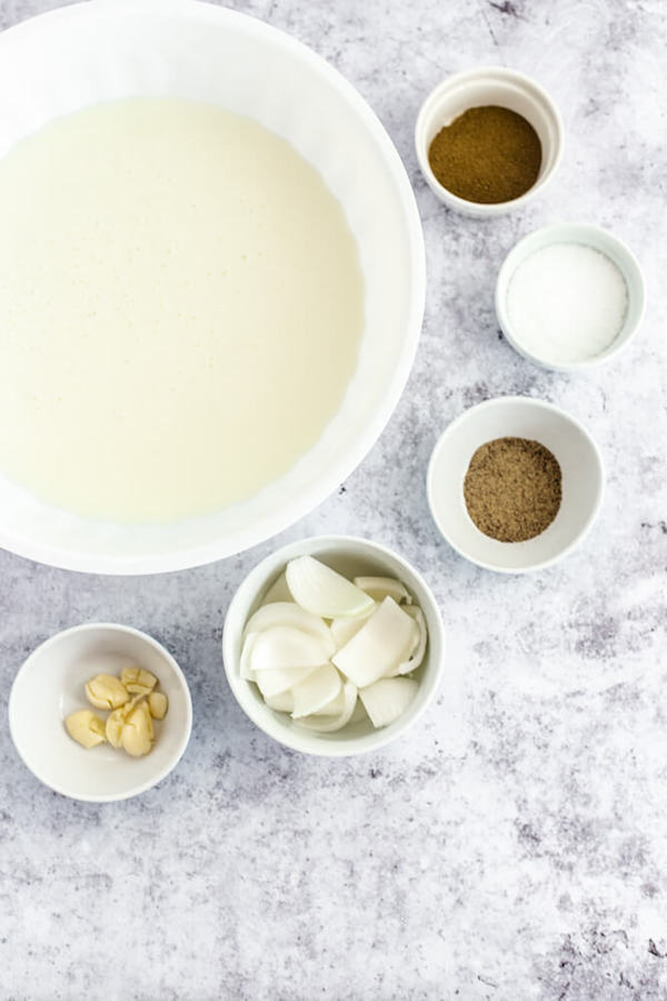 large bowl filled with buttermilk surrounded by smaller bowls filled with seasonings 