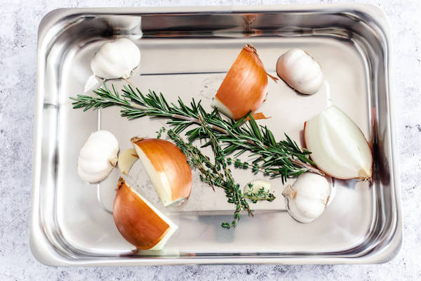 onion, garlic and herbs in a roasting pan