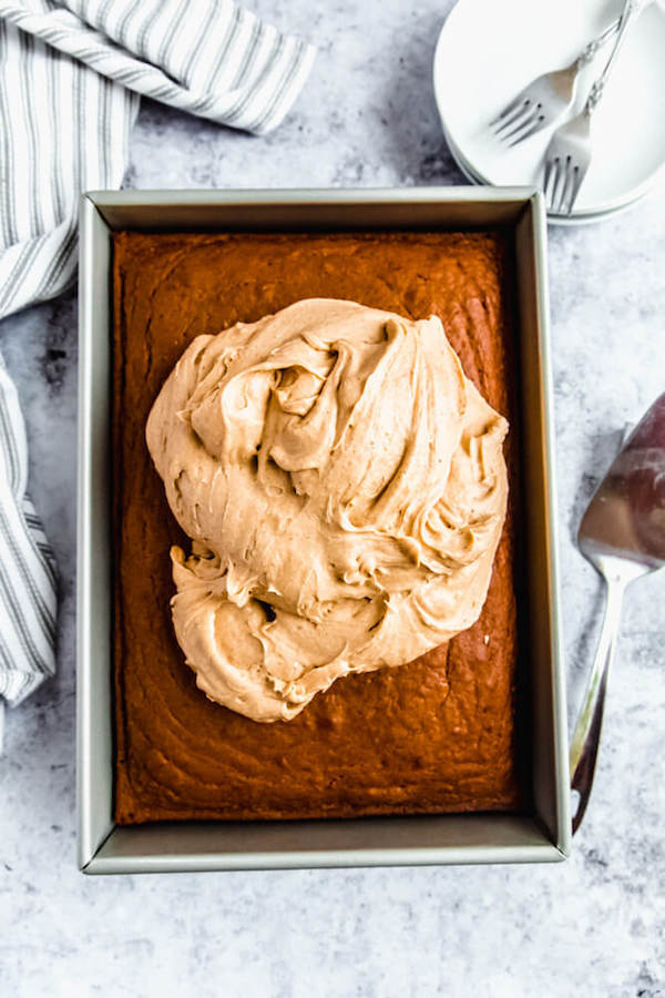 caramel pumpkin spice cream cheese frosting piled onto pumpkin sheet cake