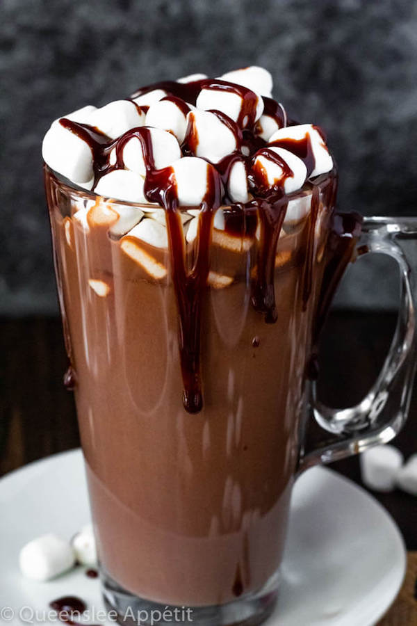 glass mug of hot chocolate topped with mini marshmallows and chocolate sauce