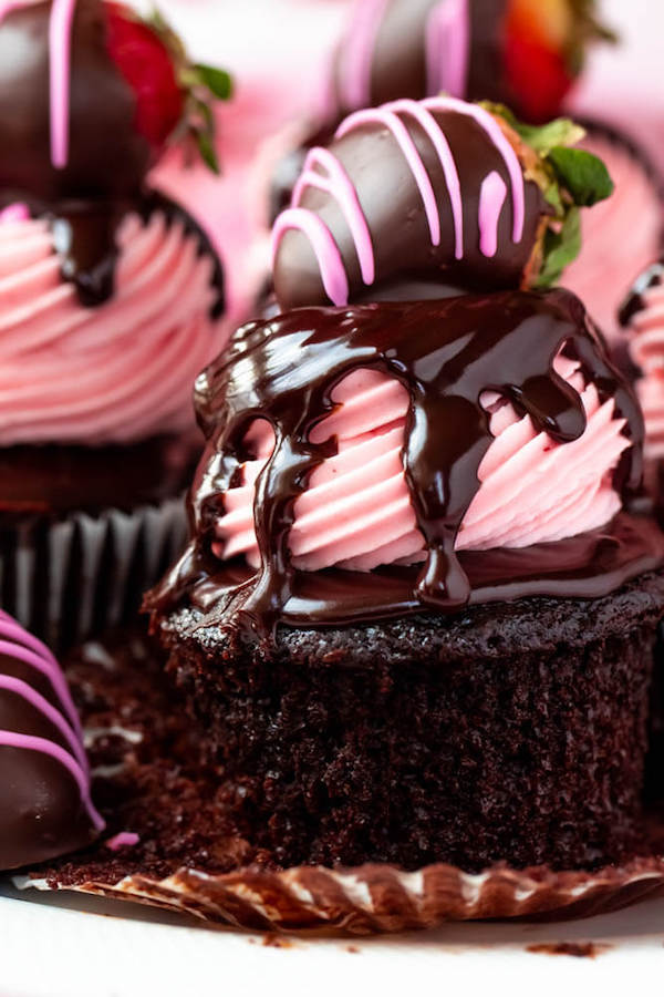 unwrapped chocolate cupcake topped with strawberry frosting and a chocolate covered strawberry