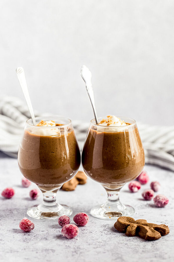 two glasses of gingerbread pudding surrounded by sugared cranberries and gingerbread men