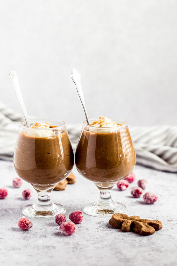 two glasses of gingerbread pudding surrounded by sugared cranberries and gingerbread men