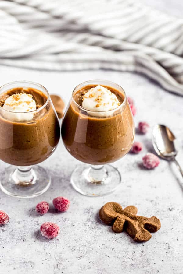 two glasses of gingerbread pudding surrounded by sugared cranberries and gingerbread men