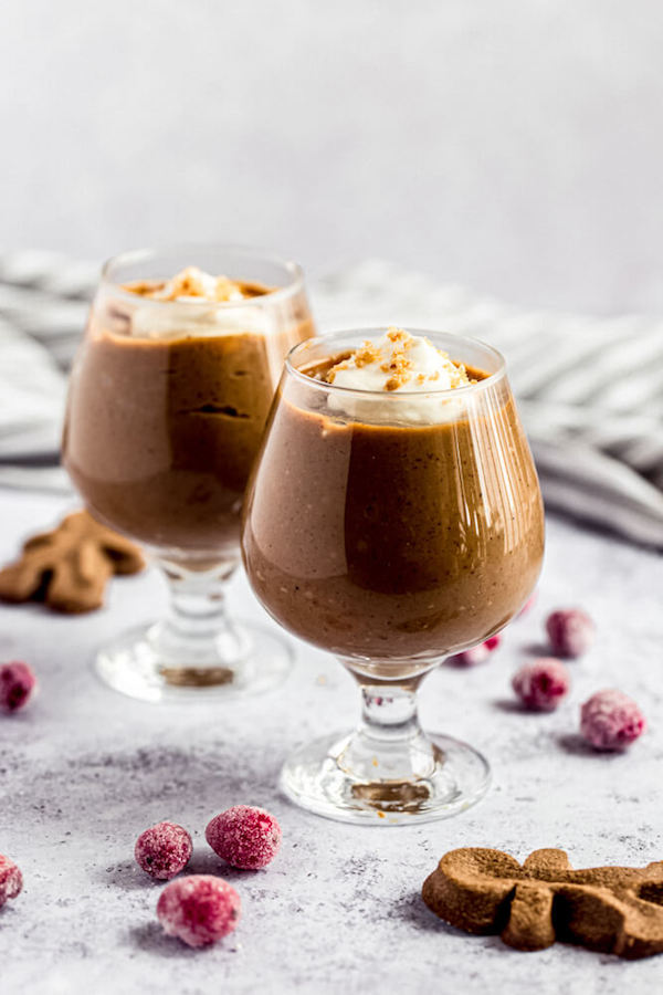 two glasses of gingerbread pudding surrounded by sugared cranberries and gingerbread men