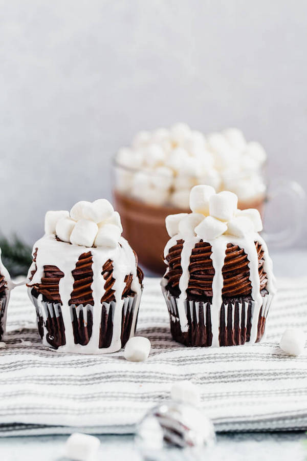 hot chocolate cupcakes on a dish towel with a mug of hot chocolate in the background