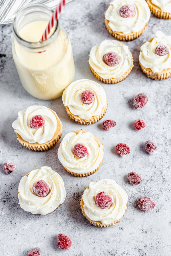 mini eggnog cheesecakes topped with sugared cranberries and a glass of eggnog