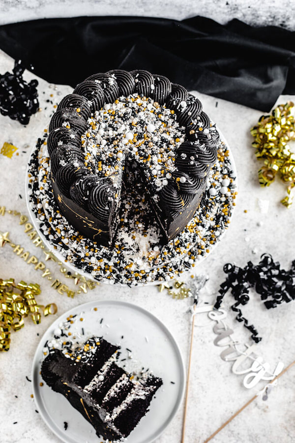 top view of black cake with gold and silver sprinkles with a slice of cake on the side
