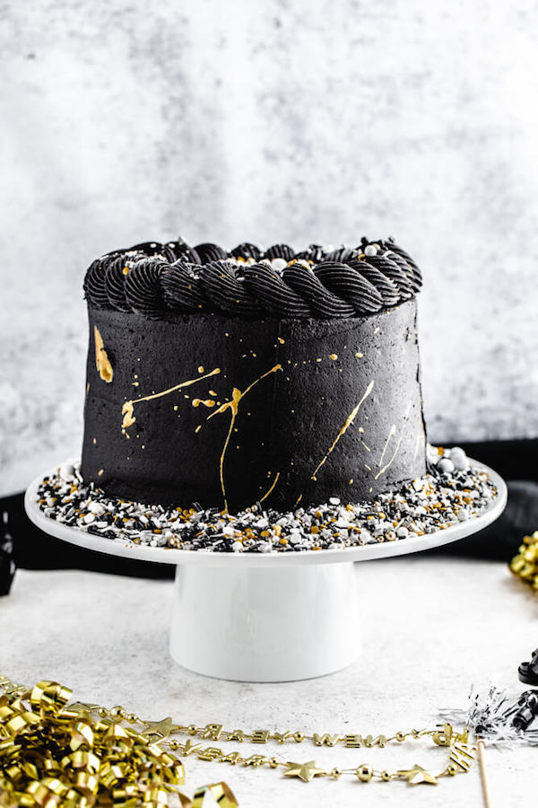 black and gold sprinkle cake on a white cake stand